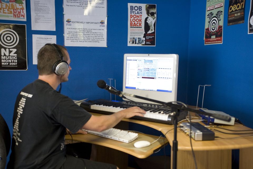 A man sits at a desk with microphone, piano keyboard, and computer